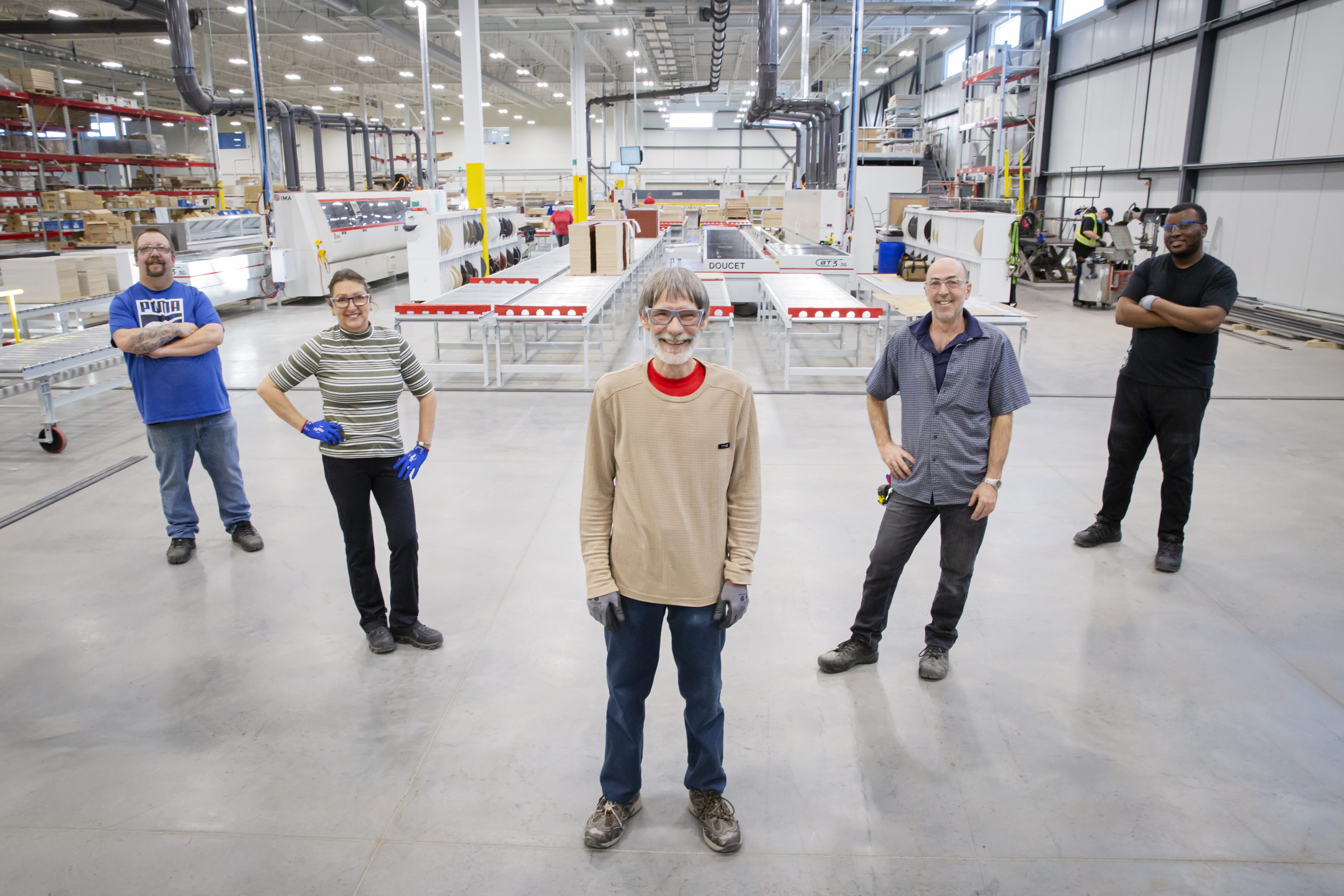 Five people standing in a factory setting with industrial equipment in the background.