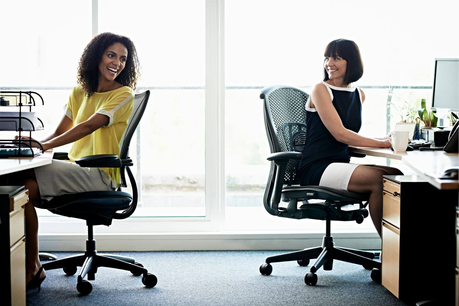 Female coworkers laughing and sitting in office chairs