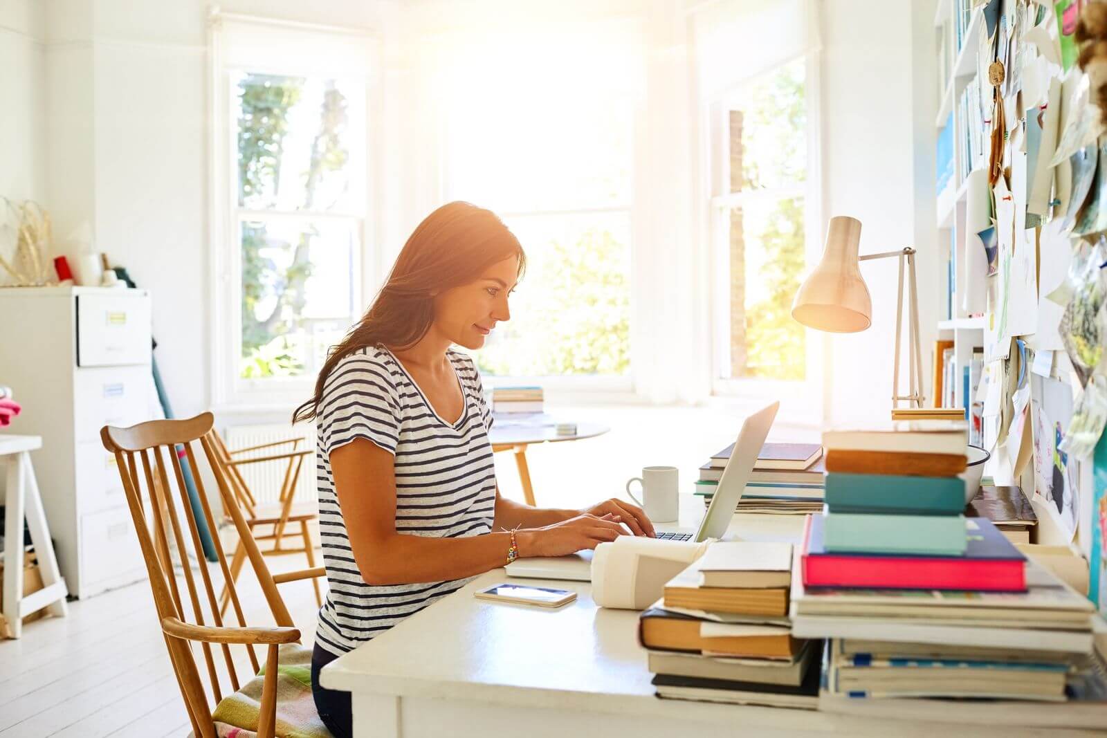 Femme assise dans un bureau à domicile, près d'une fenêtre, avec la lumière du soleil