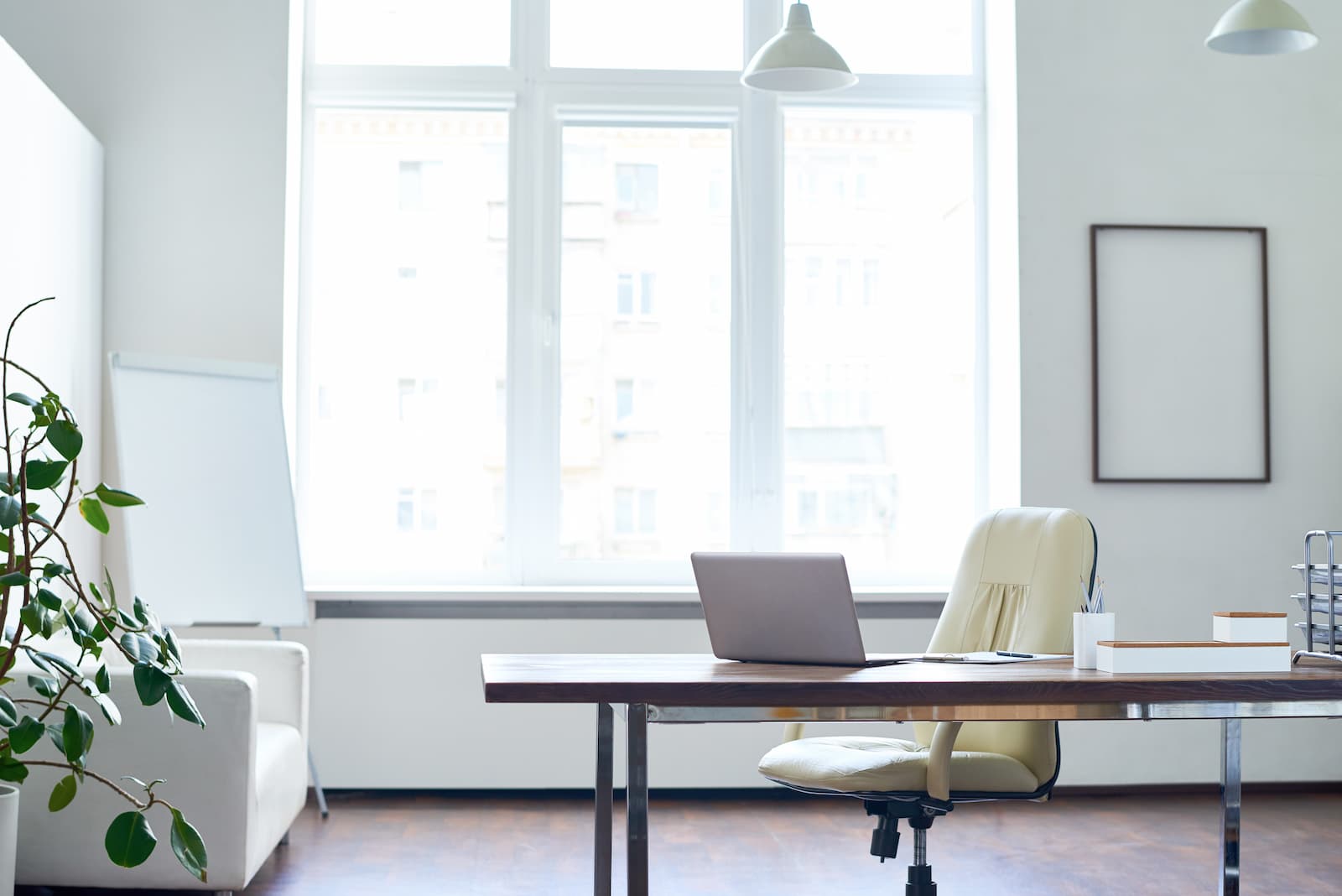 table desk with white chair and white couch next to large window