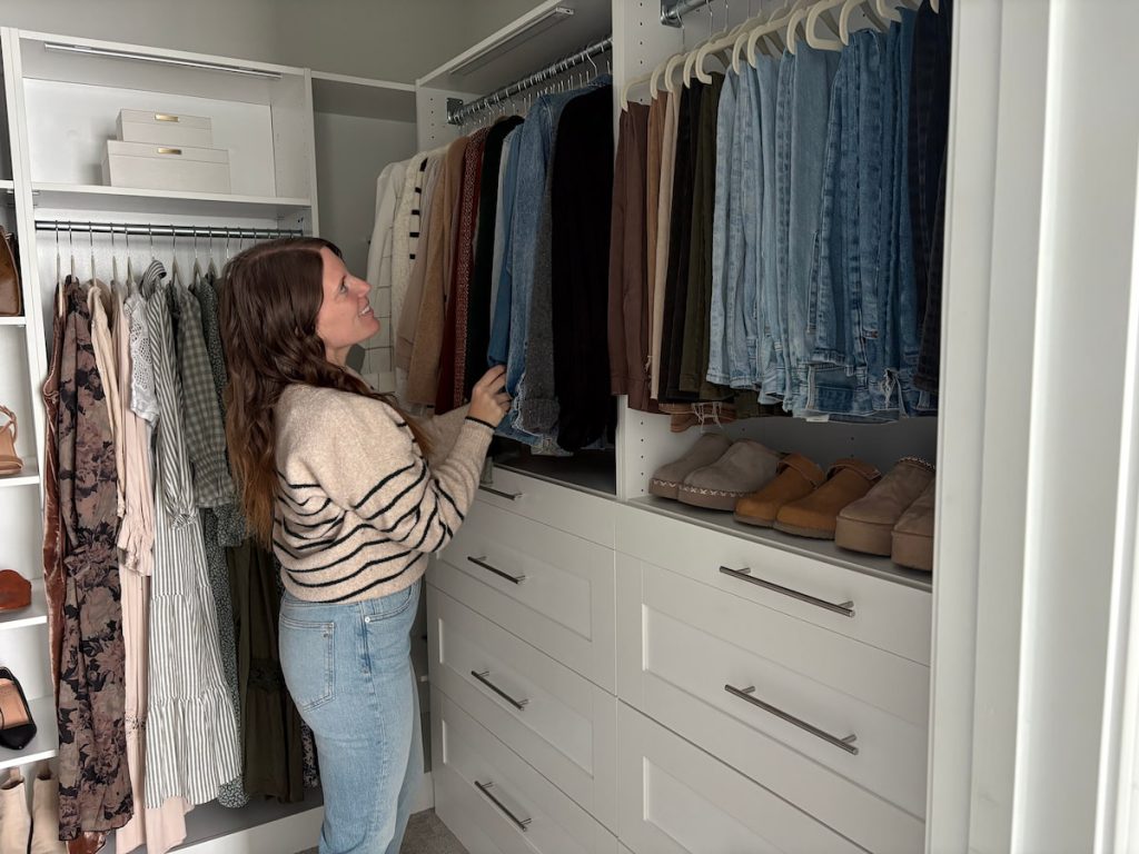 Woman organizing jeans on shelves inside a modular closet system with drawers and hangers