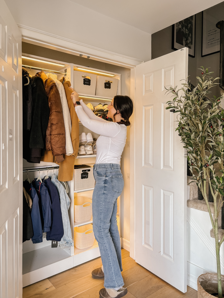 Woman organizing coats in a built-in closet with shelves and hanging rods